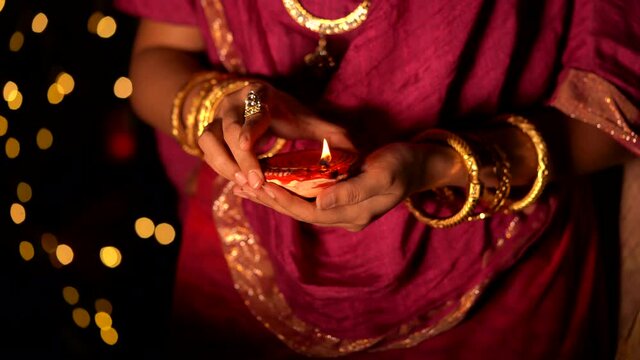 A beautiful woman or housewife holding a diya. Newly wed bride wearing traditional dress & jewellery with terracotta oil lamp on her hand during diwali celebration, Hindu retuals.