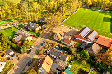 Aerial view of the edge of a village with private homes and a sports field with a green soccer field with a lawn in the corner © Frank