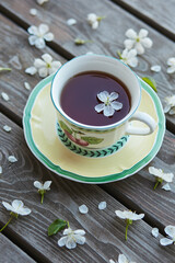 A cup of tea on a wooden background covered with cherry flowers.