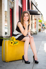 A young Armenian girl holding a yellow suitcase and yellow sunflowers in an urban setting