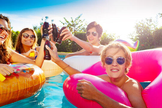 Close photo of teenage children in water party with soda drink, lift hands and swim in inflatable doughnuts