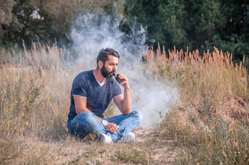 Naklejka na ściany i meble Stylish smoker enjoying an e-cigarette out in the forest. The new technology cigarette.