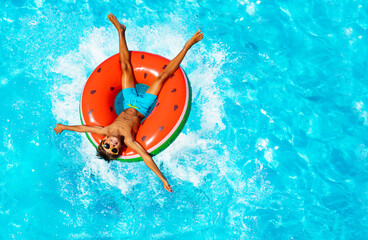 View from above of happy little boy splash and swim on inflatable watermelon ring