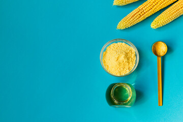 Fototapeta na wymiar Corn oil and flour in a glass bowl, fresh corn on a blue background. The concept of the production of products from corn. Top view.