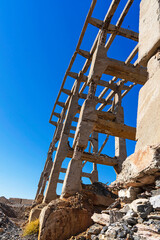 Fototapeta premium Old industrial bridge in the mountains. Destroyed mountain bridge. Abandoned concrete bridge. Concrete piles. Karatau mountains. Mountain stones. Blue sky. Mining Industrial Plant Bridge