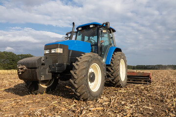 Big blue modern tractor in the field. Cultivating land after harvest