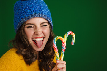 Beautiful happy girl in warm hat showing her tongue and holding candies