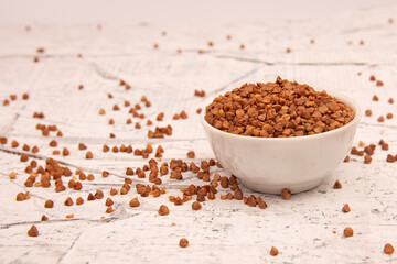 Dry buckwheat in a white ceramic bowl on a white textured background