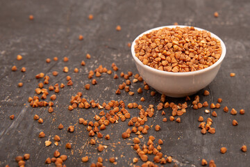 Dry buckwheat in a white ceramic bowl on a black textured background