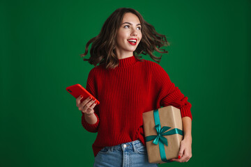Beautiful joyful nice girl posing with Christmas gift and cellphone