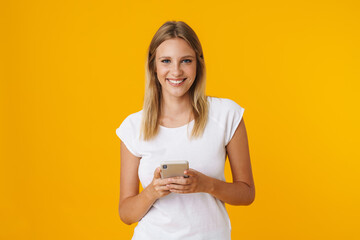 Cheerful blonde girl smiling and using mobile phone