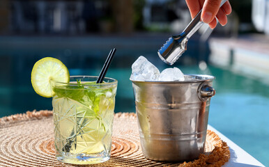 White mojito cocktail with lemon slice and ice bucket near pool