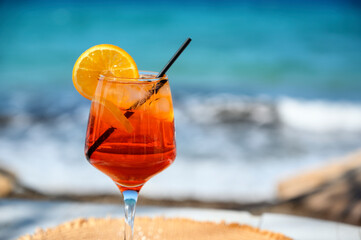 Red cocktail with orange slice and ice on a sea background