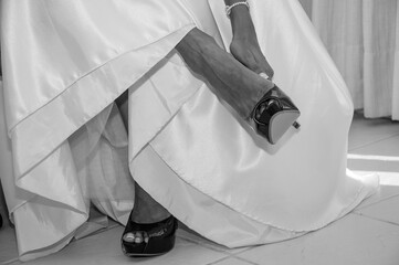 Naklejka premium Grayscale closeup shot of a female putting on shoes with a wedding dress