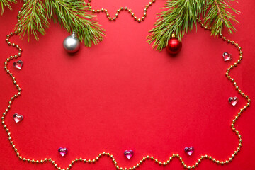 Christmas frame on a red background pine branches with decorations and decorative beads place for an inscription.