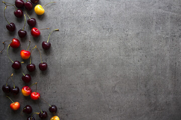 Vibrant summer frame or border made of fresh juicy cherries. Dark grey textured background with copy space. Healthy eating concept. 