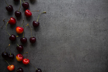 Vibrant summer frame or border made of fresh juicy cherries. Dark grey textured background with copy space. Healthy eating concept. 