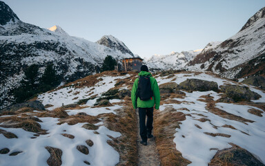Climber in a green jacket climbs a mountain against a blue sky. Hiker with backpack standing on top...