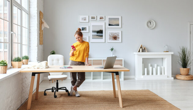 creative young woman designer in a yellow sweater in the workplace at home in interior of  apartment with large windows.