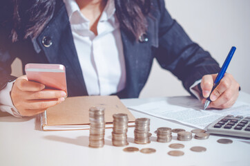 Closeup image businesswoman holding and using smartphone and calculating record or signing on business document. concept saving money wealth for finance accounting.