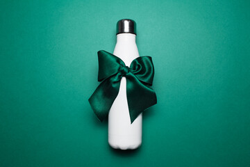 Close-up of reusable steel thermo water bottle with green bow like gift, isolated on green background.