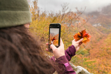 Hand holding autumn colored leaves - all shades of fall season colors with an waterfall and a river in background