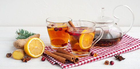 Winter warming tea. Two glass cups with tea, lemon, ginger and cranberries on a white wooden background. Banner. 