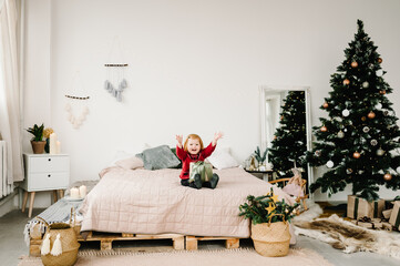 Happy little smiling girl with gift box near Christmas tree at home. The new year 2021, holidays, and childhood concept.