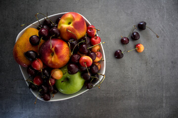 White vase with sweet cherry, nectarines, apples and mango. Grey concrete background with copy space. Juicy summer berries and fruits top view photo. Healthy eating concept. 