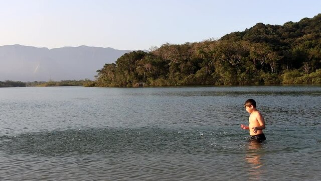 Menino se divertindo dentro do Rio e jogando água para cima. 