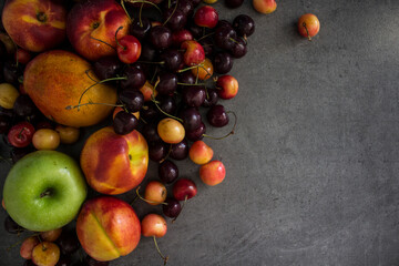 Juicy fruits and berries on a table. Dark grey textured background with copy space. Healthy eating concept. Vibrant colors of fresh fruits. 