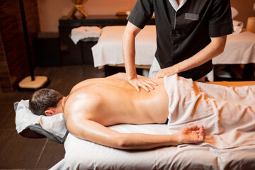 Man receiving a deep massage on his back from professional therapist at luxury spa salon