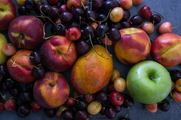 Juicy fruits and berries on a table. Dark grey textured background with copy space. Healthy eating concept. Vibrant colors of fresh fruits. 