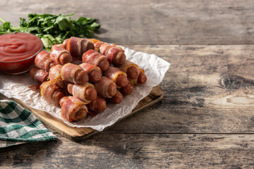 Pig in blankets. Sausages wrapped in smoked bacon on wooden table. Copy space