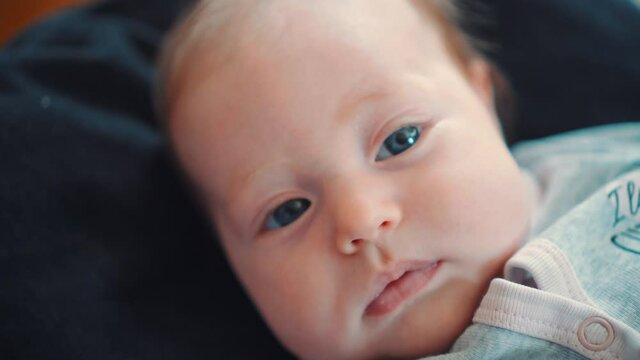 A beautiful blue-eyed newborn baby lying on a black background and looking at the camera