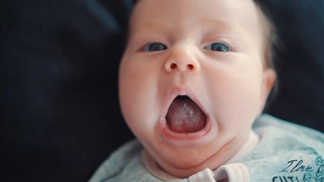 A newborn baby who is rocking and yawning lying on a black background.
