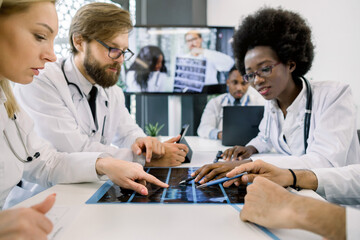 Team of international medical experts, sitting at the table on video conference, analyzing patient's CT. Young African woman and Caucasian man at digital screen, giving lecture for colleagues