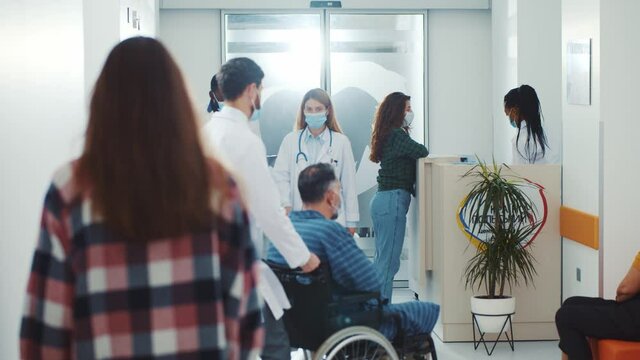 Medical Environment. Hospital. Diverse Multi-race Doctors And Assistants Walking Along The Corridor With Diseased Unhealthy Patiens. Coronavirus. Face Masks. Concept For Quarantine.