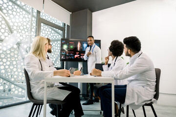 Medical education and training, teamwork concept. African male physician as a speaker in seminar, having lecture or report for his multiracial colleagues, using digital screen and schemes