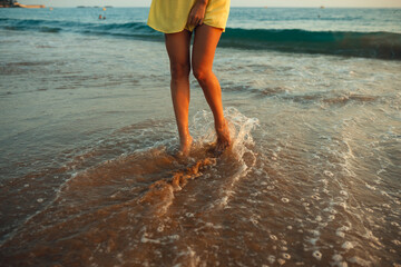 A young girl walks on the seashore in the rays of the setting sun A girl is dressed in a yellow sundress