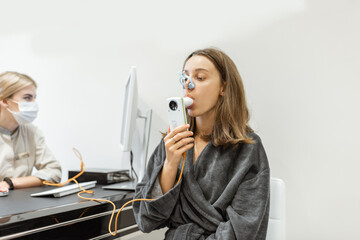 Young woman with doctor during a spirography test, measuring breathing movements with spirometer at...