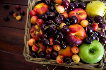 Summer fruits in basket on wooden table. Vibrant colors of beautiful cherries, apples  and nectarines. Healthy eating concept. Fresh fruits close up photo. 