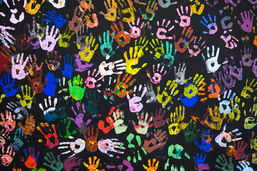 Many multi-colored prints of human hands on a black background. Peace and friendship concept. Focusing on the center of the frame.