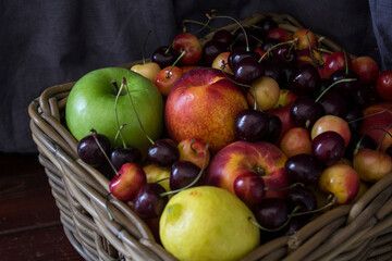 Summer fruits in basket on wooden table. Vibrant colors of beautiful cherries, apples  and nectarines. Healthy eating concept. Fresh fruits close up photo. 