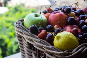 Basket full of fruits on green leaves background. JUicy summer fruits close up: cherry. apple, lemon, nectarines. Healthy eating concept. Country lifestyle. 