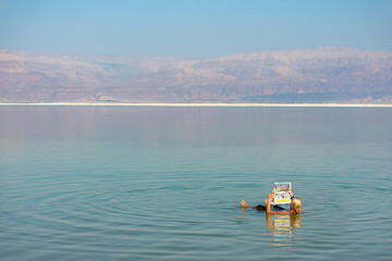 A woman floating in the water of the dead sea while reading a newspaper.