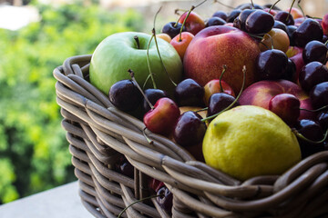 Basket full of fruits on green leaves background. JUicy summer fruits close up: cherry. apple, lemon, nectarines. Healthy eating concept. Country lifestyle. 