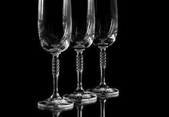 Three sparkling wine glasses stand one behind the other on a black glass surface. On the glass surface reflected the legs of the glasses. Copy space.