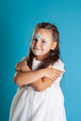 close up girl in a white Princess dress and snow petal makeup hugs her shoulders, isolated on a blue background.