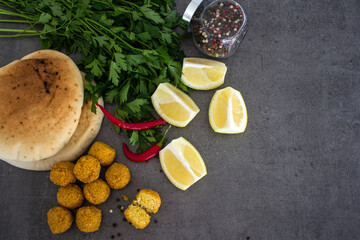 Obraz na płótnie Canvas Fresh made falafels on dark grey table with lemon slices, chili pepper and parsley. Authentic food of Israel. Ingredients top view photo. Healthy eating concept. 
